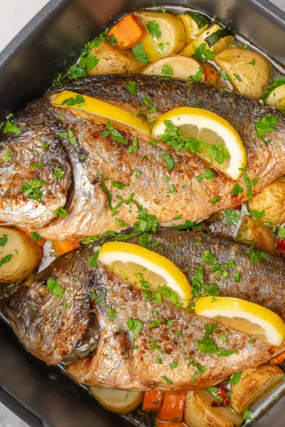 Pescados enteros dorados con limón, verduras y hierbas